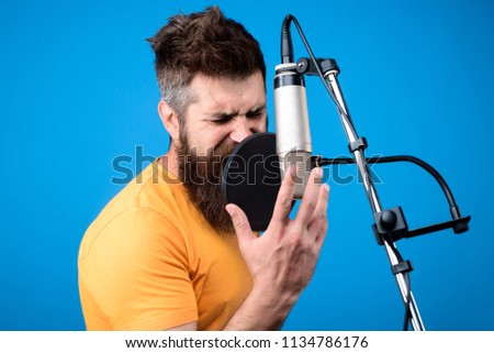 Bearded man singing into microphone in recording studio. Music. Show business. Recording studio. Male singer with microphone. Transmitter. Singing. Music and leisure concept. Close up portrait.