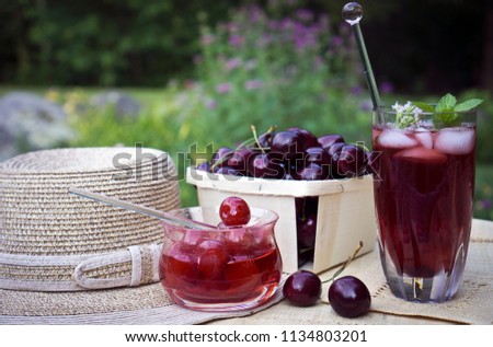 Maraschino cherries, freshly picked sweet black Cheries and iced cherry sangria on a garden table. Blossoming bee balm plants  and day lilies in the background. 