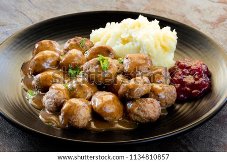 Swedish meatballs with mashed potatoes, gravy and lingonberry on black plate.  Side view, over slate. Royalty-Free Stock Photo #1134810857
