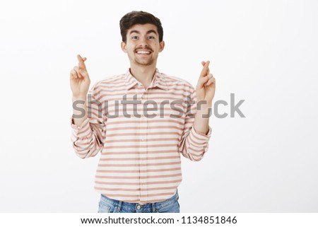 Wish me luck. Portrait of grinning friendly mature male model with moustache, crossing fingers and smiling broadly, hoping or praying for successful business deal, standing over gray background