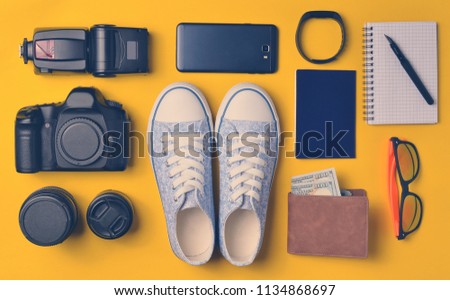 Gadgets and accessories layout on a yellow background. Sneakers, photographic equipment, purse with dollars, smart clock, smartphone, notebook, sunglasses. The concept of travel, objects, top view
