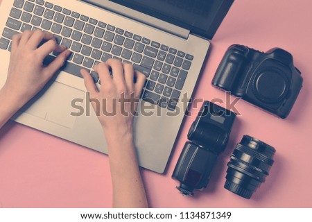 The work of the photographer, photo retouching. Photographic equipment, female hands typing on laptop keyboard on pink pastel background, top view, concept of freelancing, flat lay
