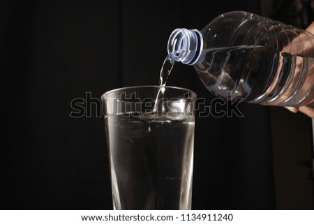 Pouring water from bottle into glass, isolated on black