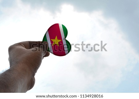 Hand holds a heart Shape Suriname flag