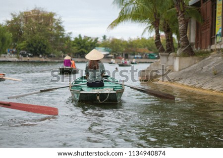 Tourists traveling in boat along the Ngo Dong River taking picture of the Tam Coc, Ninh Binh, Vietnam. Rower using her feet to propel oars. Landscape formed by karst towers and rice fields in Vietnam