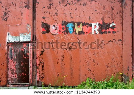 A red painted metal wall with the remnants of words attached in colorful broken letters
