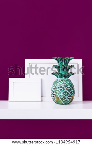 Wooden empty frames for a photo and a wooden emerald pineapple on a white shelf on a background of a bright purple red wall. Blank paper frames, modern home decor mock-up. Interior background.