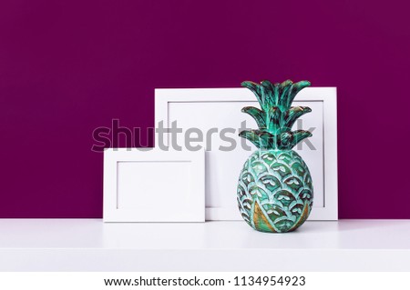 Wooden empty frames for a photo and a wooden emerald pineapple on a white shelf on a background of a bright purple red wall. Blank paper frames, modern home decor mock-up. Interior background.