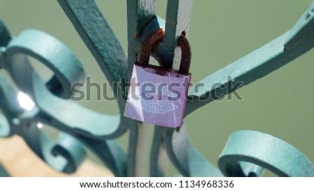 A love lock with a kiss mark, chained onto the metal rail of a bridge. A love lock or love padlock which sweethearts lock to a bridge, fence, gate, or monument, to symbolize their love.
