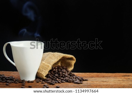 Hot coffee with smoke and seeds on wooden table, The best materials for processing fresh coffee. Coffee cup on black background