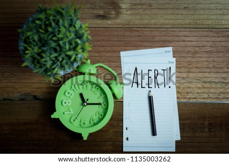 Note with text alert and alarm clock on wooden background