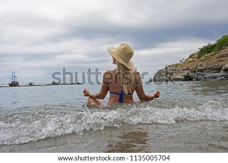 A girl sits in yoga pose in the water on the beach