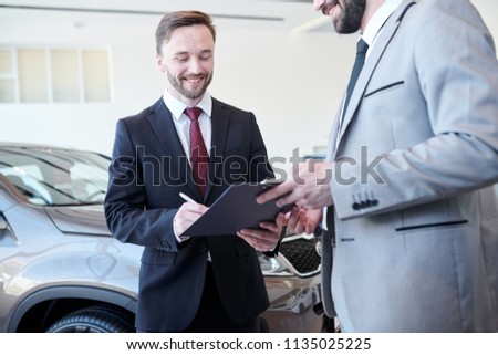 Happy bearded man concluding a contract with car dealer in auto salon