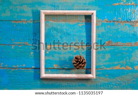 pine cone lies in a white empty frame on a blue textured wooden surface