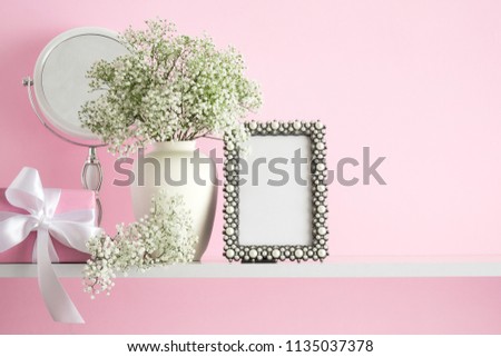 Blank mock up of photo frame on the pink background. Cosmetic set on light dressing table.Beautiful flowers in a vase on a pink wall background, gift, mirror on a wooden shelf.