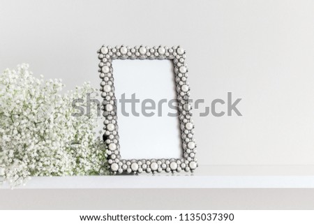 Blank mock up of photo frame on the light background. Home interior, floral decor, women's table, beautiful flowers on wall background. White flowers on a wooden shelf