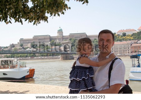 Happy father with daughter stands on the banks of the Danube river, and in the background is seen Buda Castle District (Royal Palace)