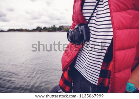 A camera on a strap on a man on a background of a landscape with water, an image with a retro toning. Travel, blogging, reporting, art and creativity concept