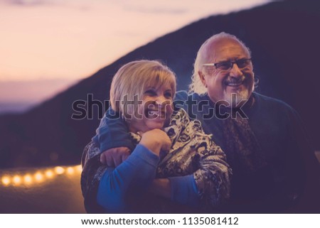man and woman senior gentlemens aged in love hug and have fun smiling on the rooftop in vacation at home. night light atmosphere for romantic scene. together forever concept and smiles
