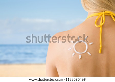 Sun shape created from sunscreen lotion on young woman's back. Skin protection. Hot day. Safety sunbathing concept. Copy space. Empty place for text on beach background. Royalty-Free Stock Photo #1135090469