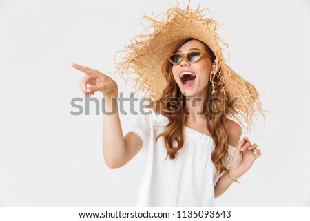 Photo of excited stylish girl 20s wearing big straw hat and sunglasses pointing finger at copyspace isolated over white background