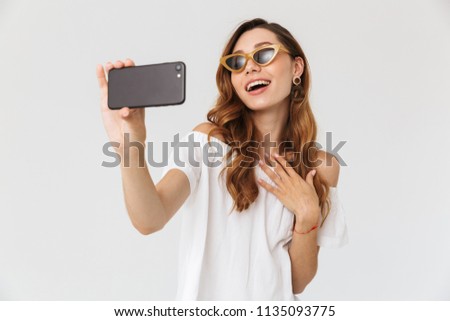 Photo of cheerful stylish woman 20s wearing sunglasses and jewelry taking selfie on smartphone isolated over white background