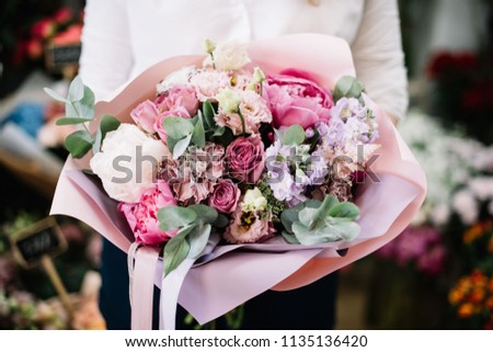 Very nice young woman holding beautiful blossoming flower bouquet of fresh matthiola, peonies, eustoma, eucalyptus, roses in pink colors on the flower stalls background at the florist shop