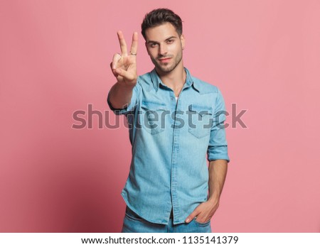 casual man makes peace sign while holding his pocket and standing on red background, portrait picture
