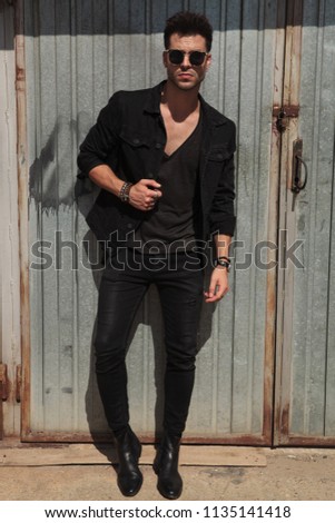 handsome man in black clothes standing outside near garage door, full body picture