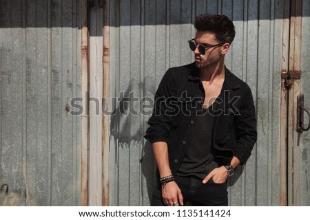 casual man with sunglasse standing in front of metal door looks to side, portrait picture