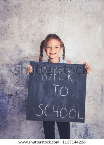 schoolgirl is holding blackboard with the words back to school in front of concrete background