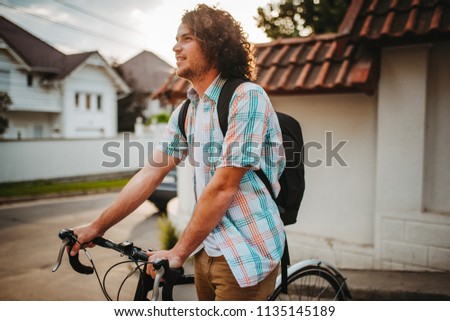 Young handsome hipster male with curly hair with backpack, ride the bike on the city street for ecological life. Man student bicycling with bycicle to the college. People, lifestyle and sport