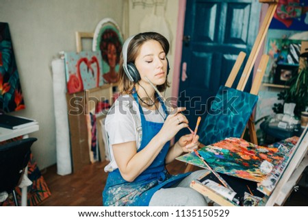 Young beautiful woman drawing something on  canvas and listening