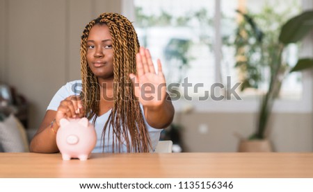 African american woman saving money with piggy bank with open hand doing stop sign with serious and confident expression, defense gesture