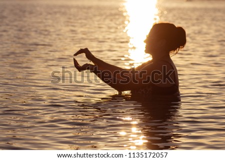 Silhouette of a woman in the water at the sea at sunset