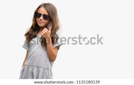 Brunette hispanic girl wearing sunglasses doing happy thumbs up gesture with hand. Approving expression looking at the camera with showing success.