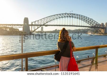 Female tourist with backpack bag  taking photos of Sydney Harbour Bridge during summer vacation trip.