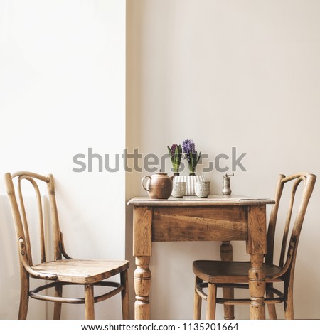 Vintage interior design of kitchen space with small table against white wall with simple chairs and plant decorations. Minimalistic concept of kitchen space.