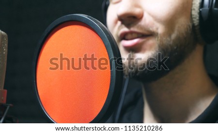Unrecognizable male singer in headphones singing song at sound studio. Young man emotionally recording new melody or song. Working of creative musician. Show business concept. Slow motion.