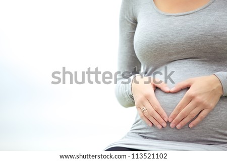 Pregnant woman caressing her belly and making a heart shaped gesture with her fingers signifying her love for her unborn child Royalty-Free Stock Photo #113521102