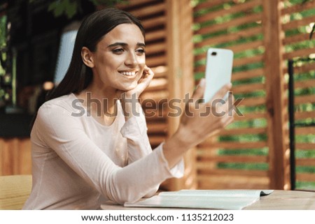 Smiling young girl taking a selfie with mobile phone while sitting at a cafe outdoors
