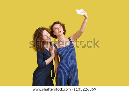 Joyful female curly friends or shaggy hair sisters take picture on modern smart phone spend happy and fun time together. Cheerful young woman holds cellular for making photo. Selfie. Modern technology