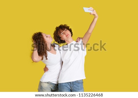 Joyful female curly friends or shaggy hair sisters take picture on modern smart phone spend happy and fun time together. Cheerful young woman holds cellular for making photo. Selfie. Modern technology