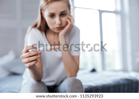 Unexpected result. Unhappy pretty woman sitting and holding her pregnancy test