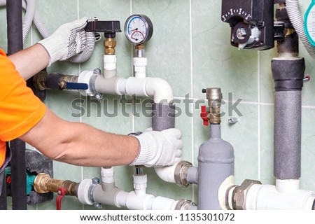 A worker or an engineer checks the operation of the heating system in a room with engineering communications in an apartment building. Royalty-Free Stock Photo #1135301072