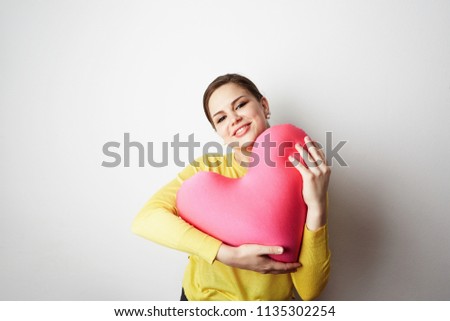 Young beautiful girl in yellow tshirt holding big plush red heart over empty white background.Lifestyle and Holiday Concept