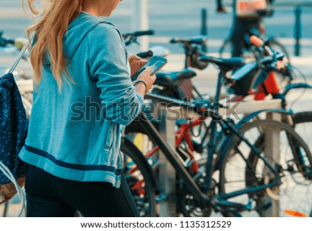 Woman wearing blue shirt texting on the smart phone walking in the street in a sunny day. 