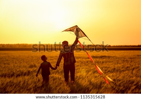 Happy father and son flying kite in the field at sunset Royalty-Free Stock Photo #1135315628