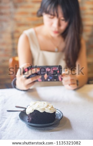 woman taking picture of dark chocolate cake with cream cheese on the table.