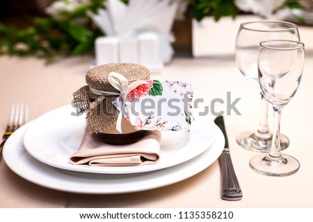 gift confiture decorated with a ribbon and a sackcloth as a present for guests standing at a wedding party table on the plate near glasses. concept of bridal presents Royalty-Free Stock Photo #1135358210